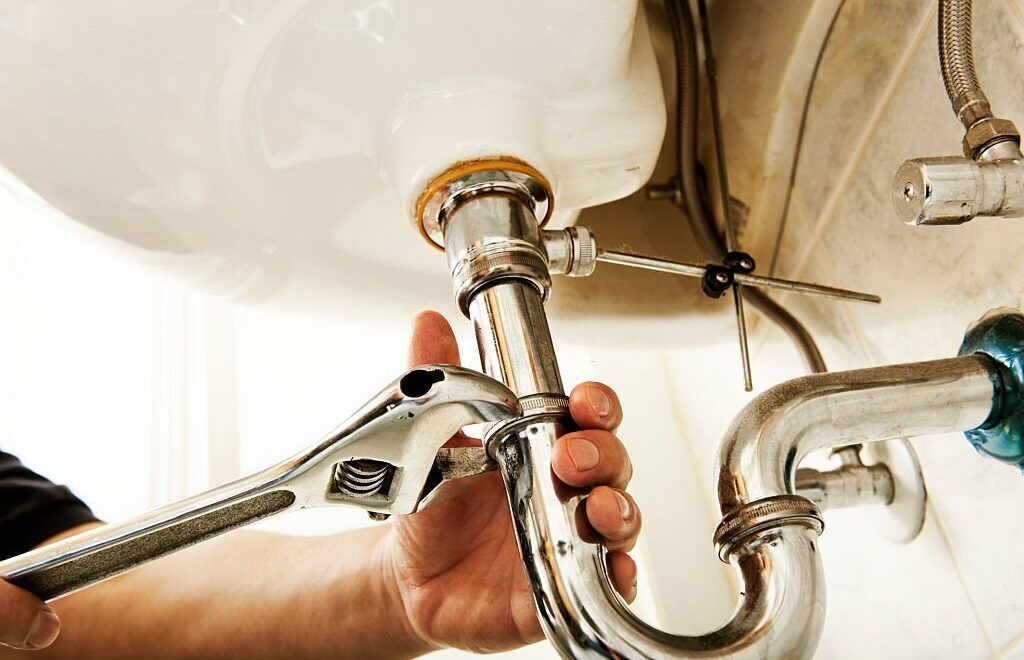 Plumber using a wrench to tighten a siphon under a sink