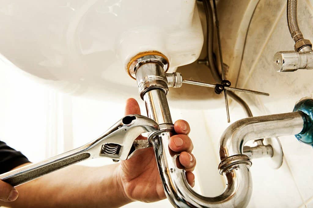 Plumber using a wrench to tighten a siphon under a sink